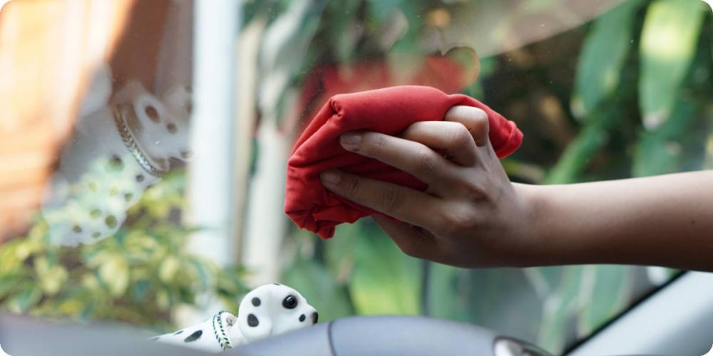 Eine Hand wäscht mit einem roten Mikrofasertuch die Innenseite der Frontscheibe.