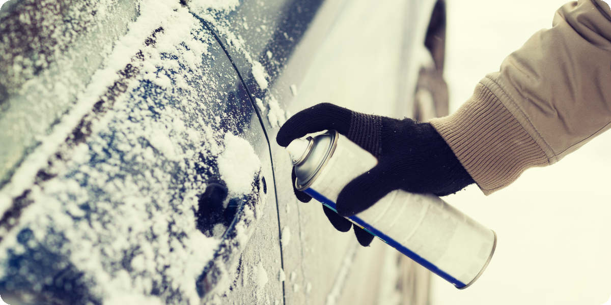 Eine Person spr&uuml;ht ein Enteisungsspray auf eine zugefrorene Autot&uuml;r. 