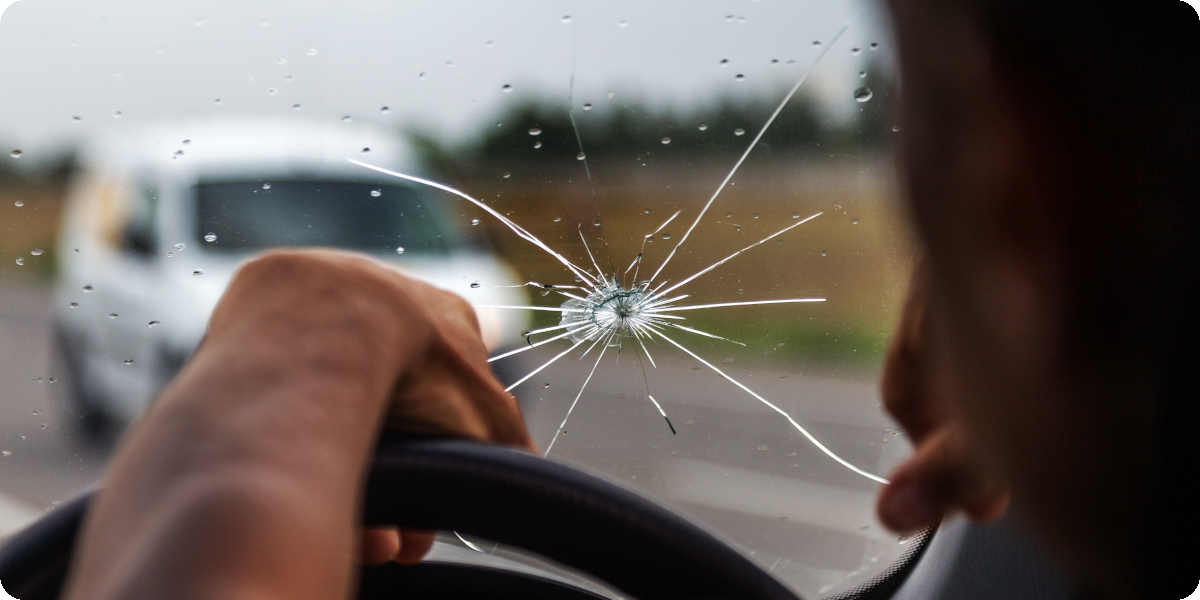 Ein Mann sitzt am Steuer eines Autos mit gesprungener Windschutzscheibe aufgrund eines Steinschlags.